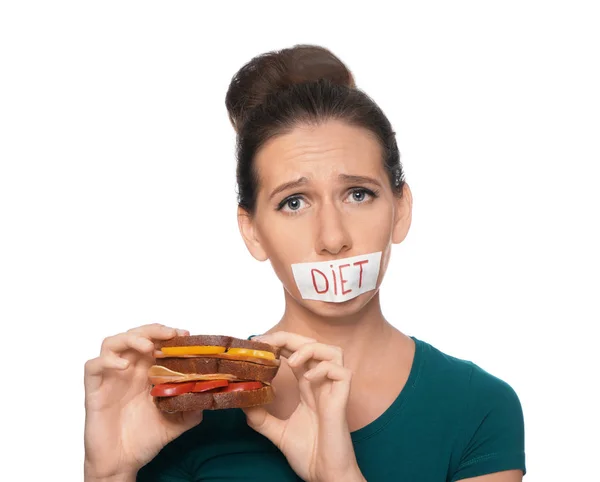 Woman with taped mouth and tasty sandwich on white background. Diet concept