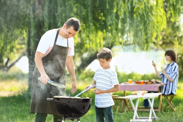 小男孩与他的父亲烹调美味的食物在烤肉烧烤户外 — 图库照片