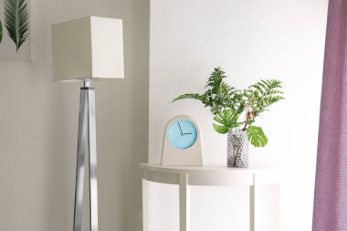 Tropikal yapraklarda hafif duvarının kapalı yakınında tablo vazo ile masa saati içinde