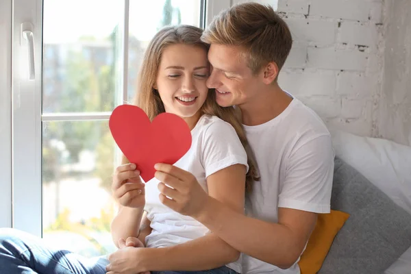 Šťastný Mladý Pár Červeným Srdcem Sedící Okna Doma — Stock fotografie