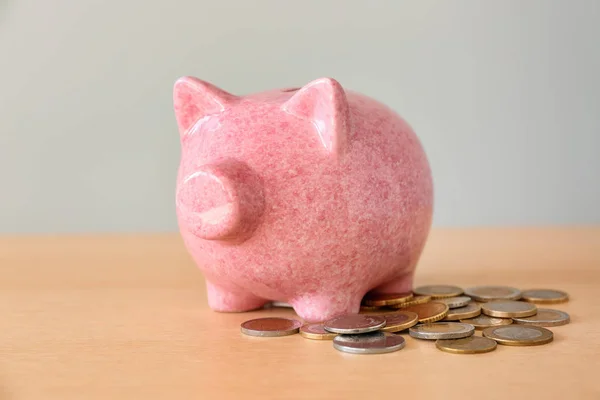 Piggy bank with coins on light wooden table