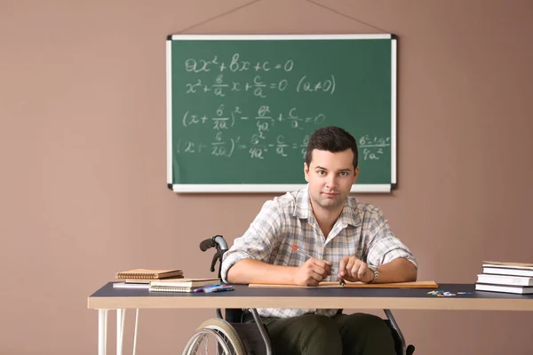 Male teacher in wheelchair working at table in classroom
