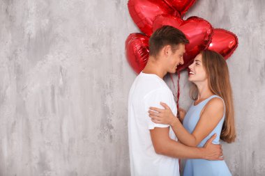 Gri duvarının yakınında kırmızı balon şeklinde kalbi olan genç çift