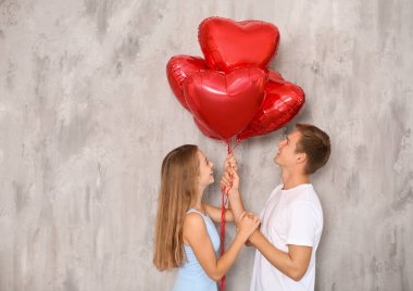 Gri duvarının yakınında kırmızı balon şeklinde kalbi olan genç çift