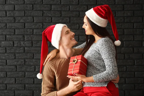 Bonito Jovem Casal Com Presente Natal Contra Parede Tijolo Escuro — Fotografia de Stock
