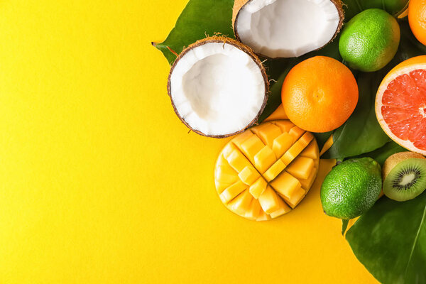 Различные вкусные экзотические фрукты с тропическими листьями на цветном фоне
