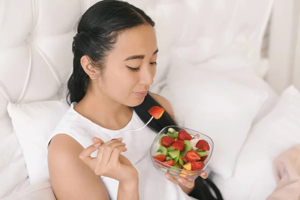 Asian woman eating healthy fruit salad for breakfast at home