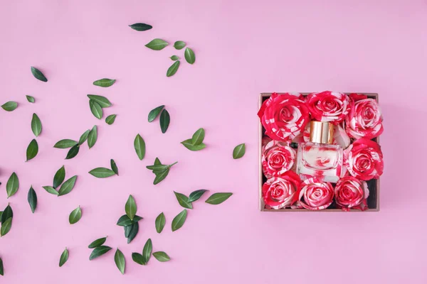 Box with bottle of perfume and roses on color background