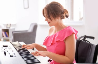 Evde synthesizer oynarken tekerlekli sandalyede güzel genç müzisyen