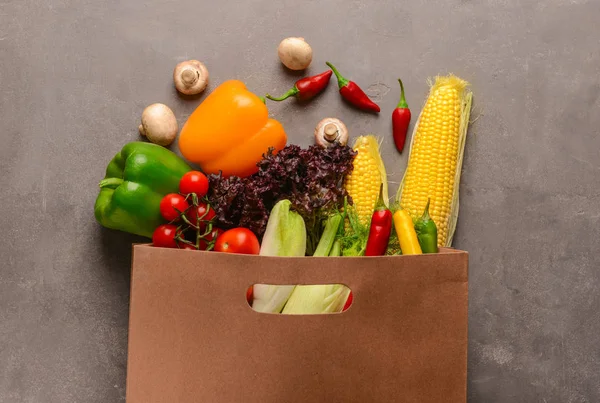 Paper bag with various fresh vegetables on grey background