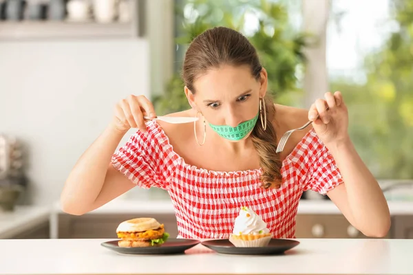 情绪化的女人 她的嘴巴周围有卷尺 厨房里不健康的食物 饮食理念 — 图库照片