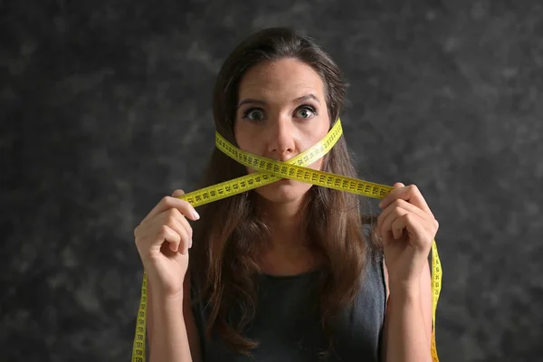 Woman with measuring tape around her mouth on dark background. Diet concept