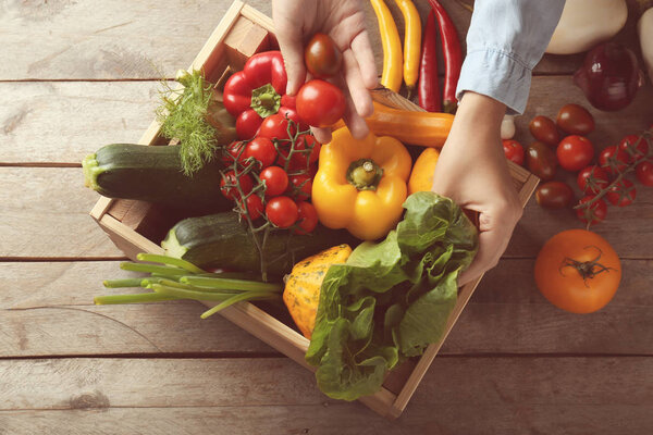 Woman taking fresh vegetables out of wooden crate, top view
