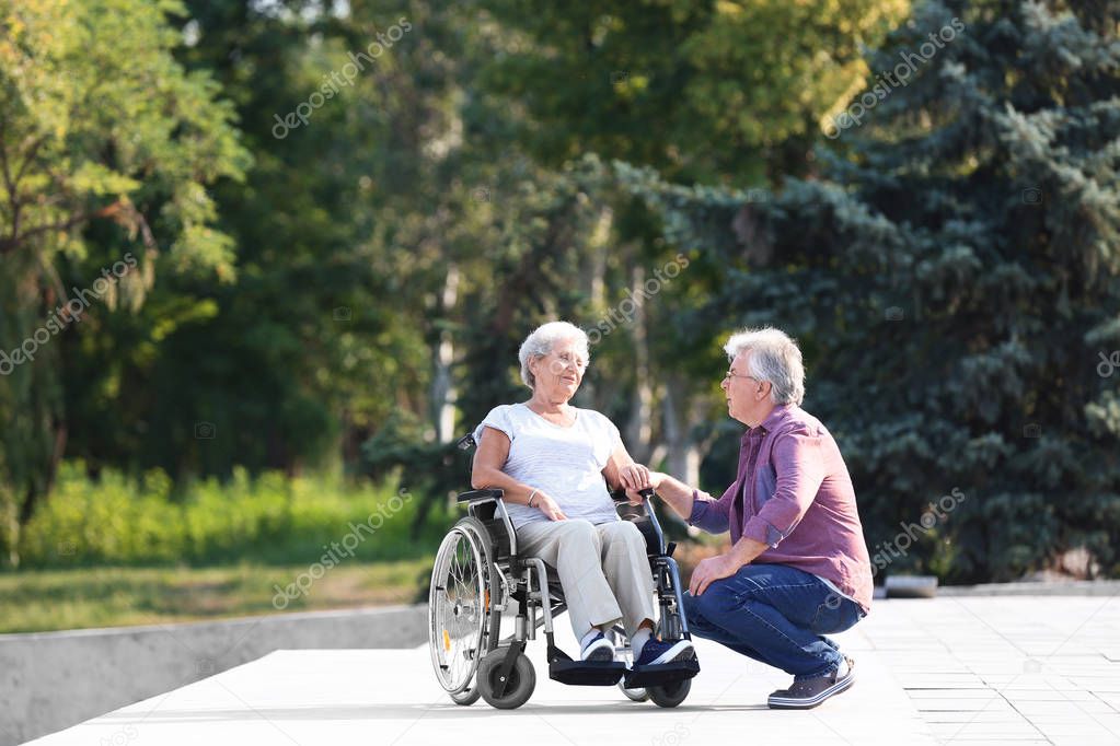 Senior woman in wheelchair and her husband outdoors