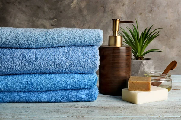 Clean soft towels with cosmetics on light wooden table