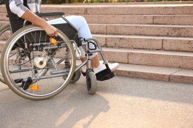 Dışarıda merdivenlerin yanında tekerlekli sandalyede genç bir kadın var.