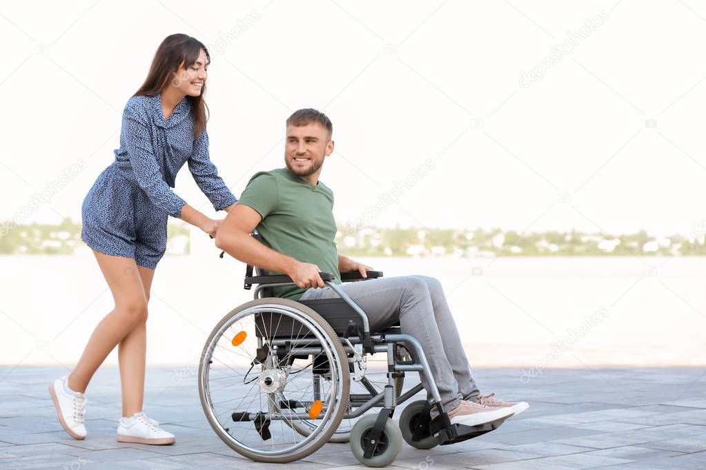 Happy young man in wheelchair and his wife outdoors