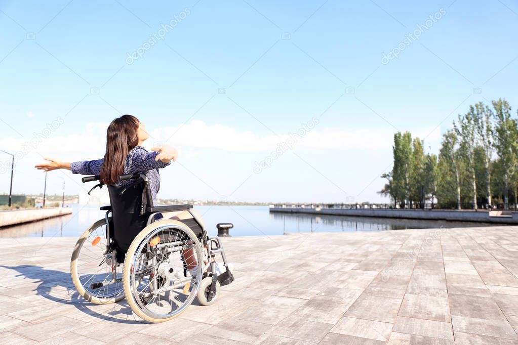 Happy young woman in wheelchair outdoors