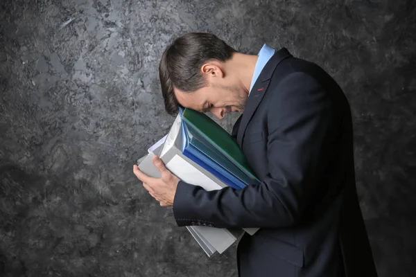 Handsome stressed businessman with documents on dark background