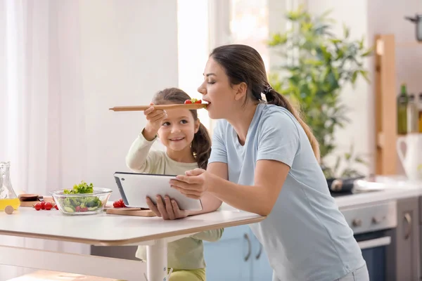Mother and daughter with tablet PC reading recipes in kitchen