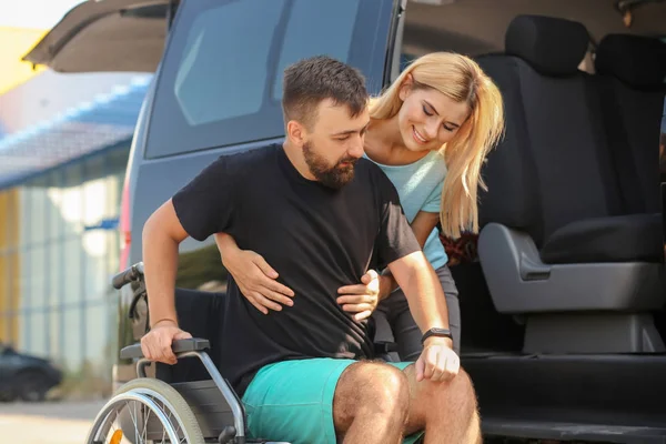 Woman helping handicapped man to sit in car