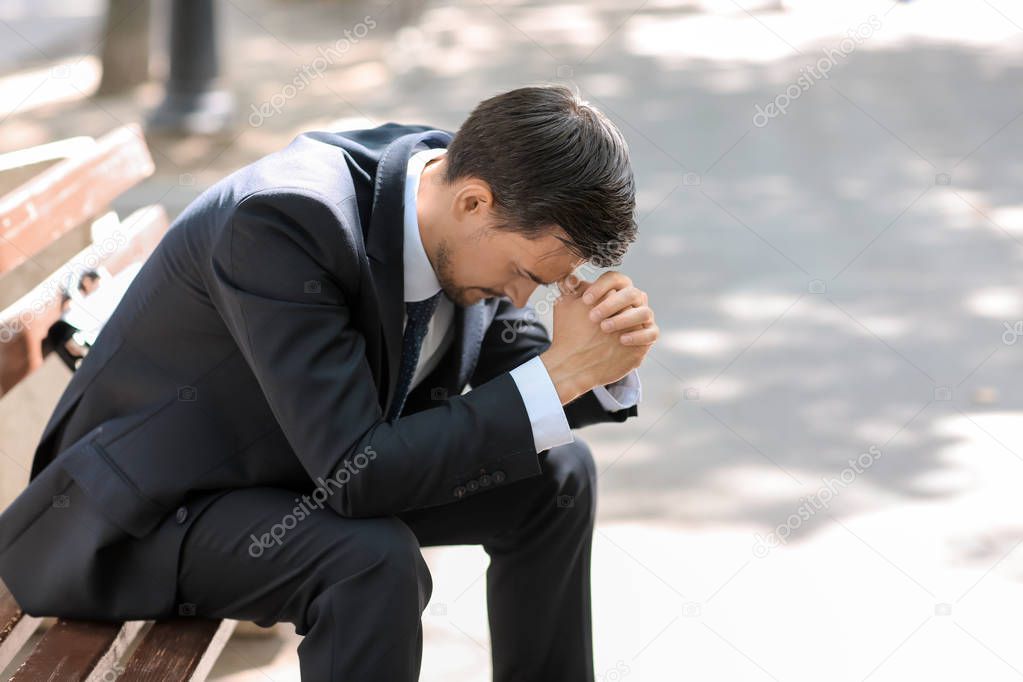 Handsome stressed businessman sitting on bench outdoors