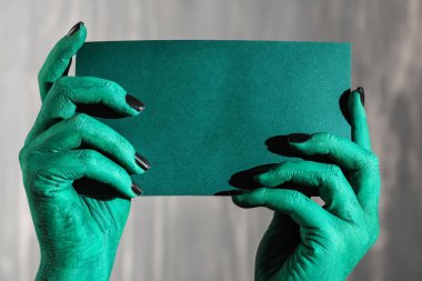 Boş kartı gri arka plan üzerinde tutan canavar