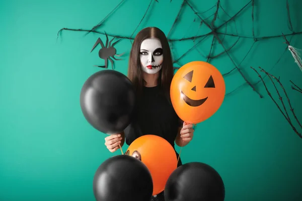 Beautiful woman dressed for Halloween with balloons standing near decorated wall