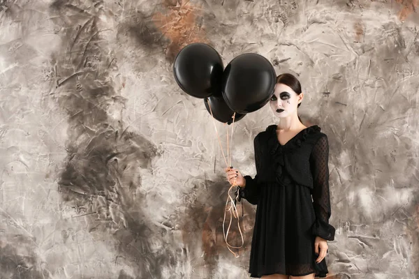 Beautiful woman dressed for Halloween with balloons standing near color wall