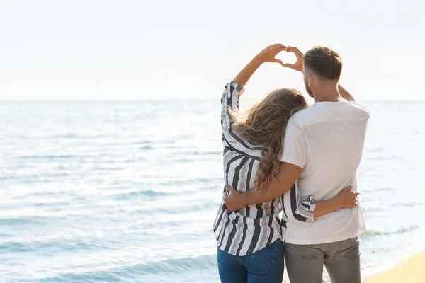 海岸で手でハートを作るかわいい若いカップル — ストック写真