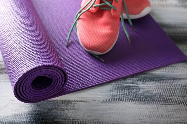 Yoga mat with sport shoes on wooden background