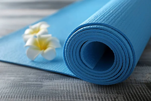 Color yoga mat and flowers on wooden background