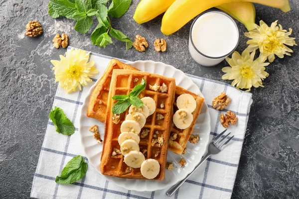 Delicious waffles with banana slices and glass of milk on grey table
