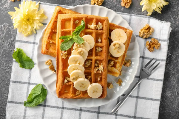 Delicious waffles with banana slices and nuts on plate