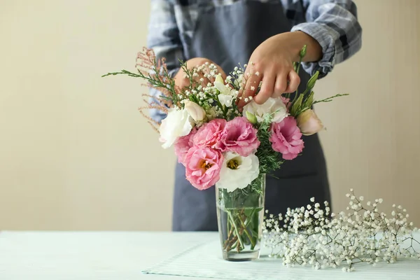 Florist making bouquet of beautiful flowers at light table