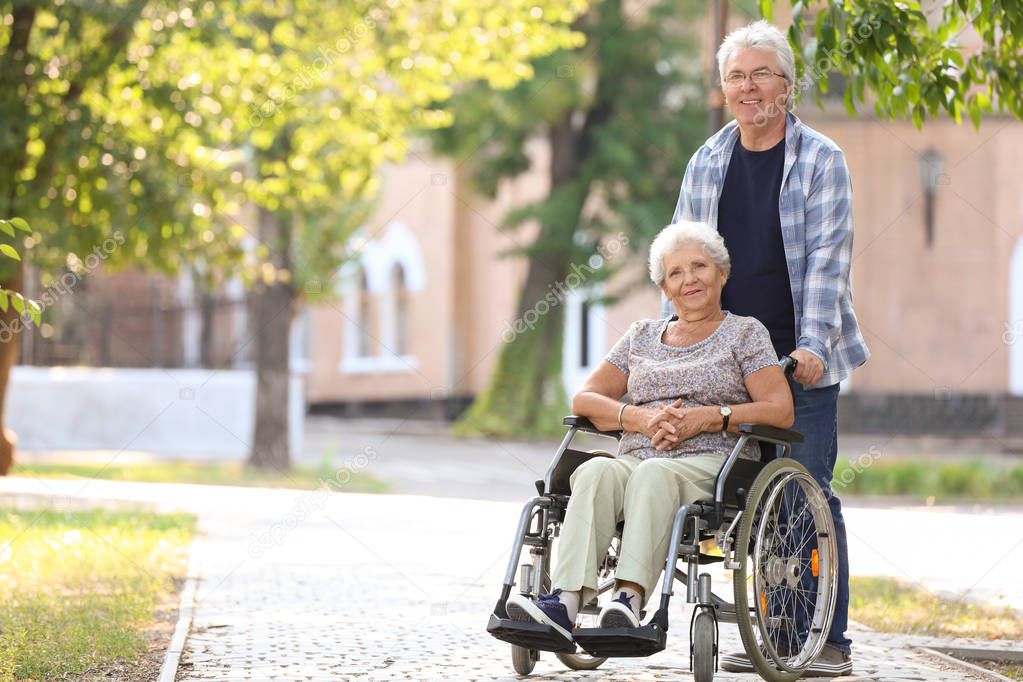 Senior woman in wheelchair and her husband outdoors