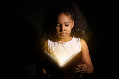 Küçük Afrikalı-Amerikalı kız koyu arka plan üzerinde sihirli kitap okuma
