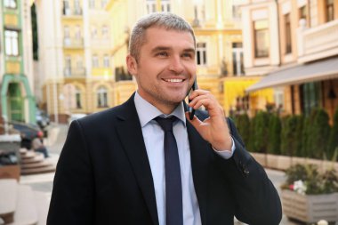 Dışarıda cep telefonuyla konuşan yakışıklı bir iş adamı.