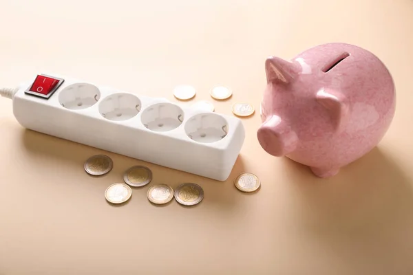 Piggy bank with coins and extension cord on color background. Electricity saving concept