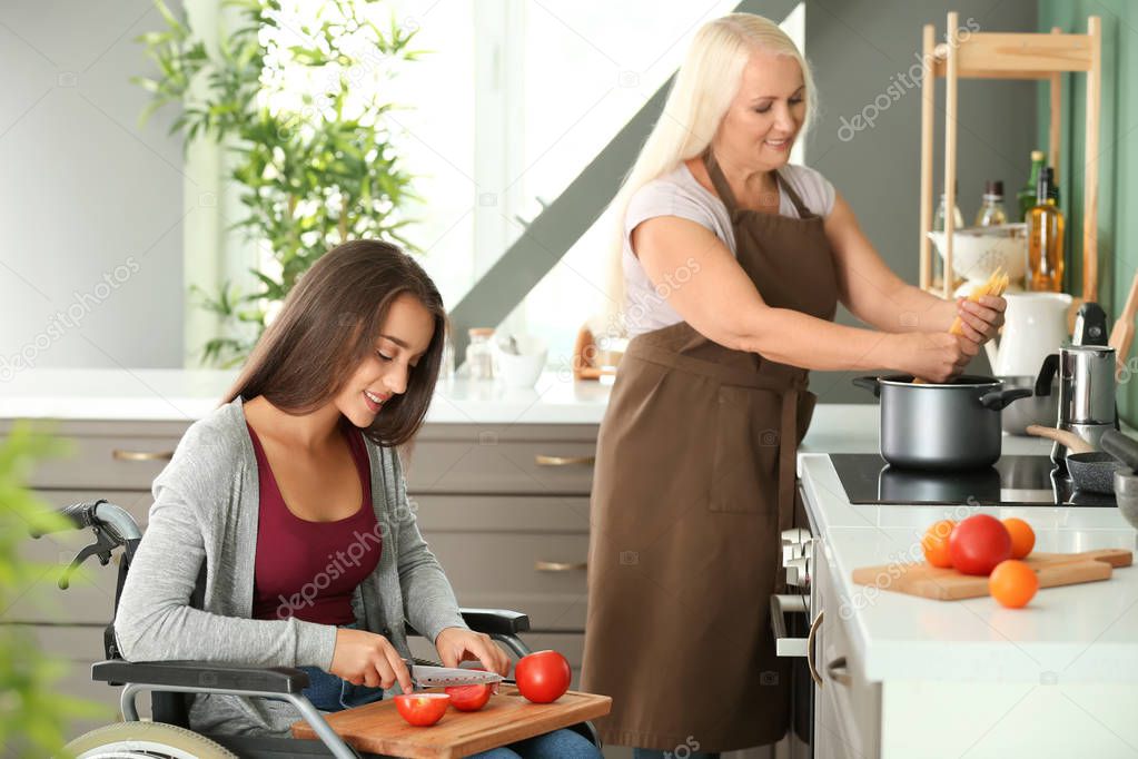 Young woman in wheelchair cooking together with her mother