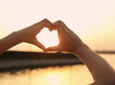 Sevimli küçük çocuk kalp el ile açık havada günbatımında yapma