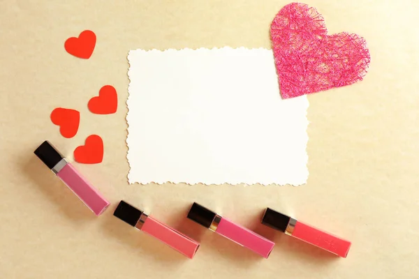 Liquid lipsticks with blank card and red hearts on color background