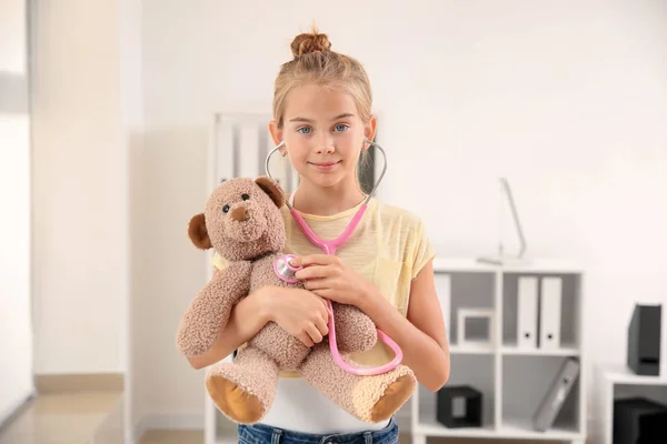 Cute little girl with stethoscope and teddy bear at home