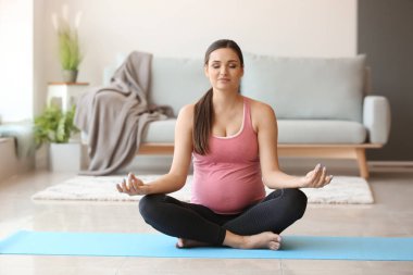 Genç hamile kadın evde yoga yapıyor.