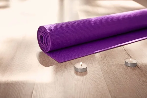 Yoga mat and burning candles on floor