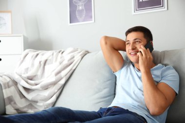 Genç adam evde cep telefonuyla konuşuyor.