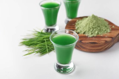 Bardak taze buğday çimen suyu toz beyaz arka plan üzerinde ahşap tahta yakınındaki