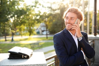 Yakışıklı genç işadamı parkta cep telefonuyla konuşuyor.