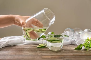 Lezzetli salatalık su sürahi içine Kupası ahşap masa üzerinde üzerinden dökme kadın