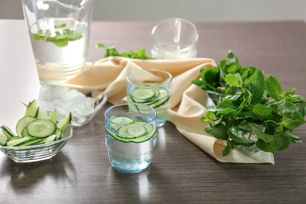 Glasses of tasty fresh cucumber water with ingredients on wooden table